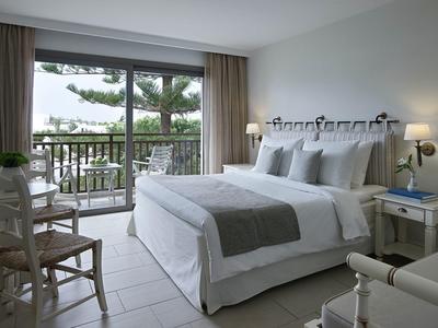 Chambre d'hôtel lumineuse avec grand lit, balcon et vue sur des arbres verts.