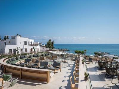 Terras met zitplaatsen en zeezicht bij een hotel onder een heldere lucht.