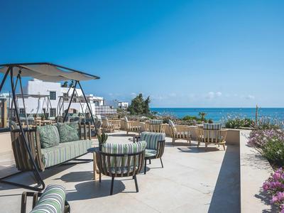 Salon extérieur moderne avec sièges, vue sur la mer et ciel dégagé en arrière-plan.