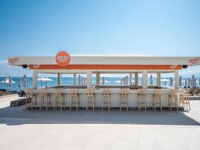 Espace bar de plage moderne avec tabourets et parasols sous un ciel clair