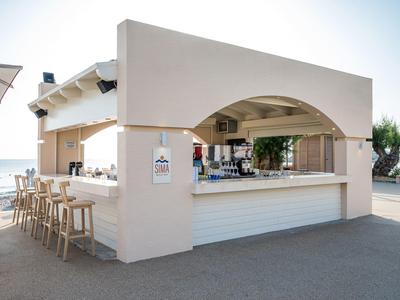 Bar de plage ouverte avec tabourets, sièges et vue sur la mer en plein jour.