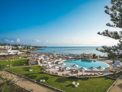 Grande piscina con ombrelloni e lettini in un giardino curato vicino al mare.