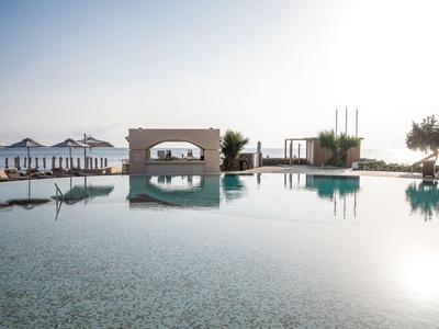 Piscine à débordement avec vue sur la mer et parasols de plage sous un ciel clair.