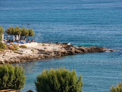 Küstenlandschaft mit Felsen, Bäumen und blauen Sonnenschirmen am Meer