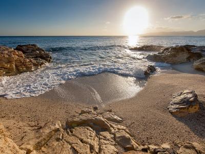 Strand mit Felsen und Sonnenuntergang über ruhigem Meer.