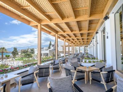 Überdachte Terrasse mit Holzbalken, Stühlen und Tischen mit Blick auf das Meer und Palmen.