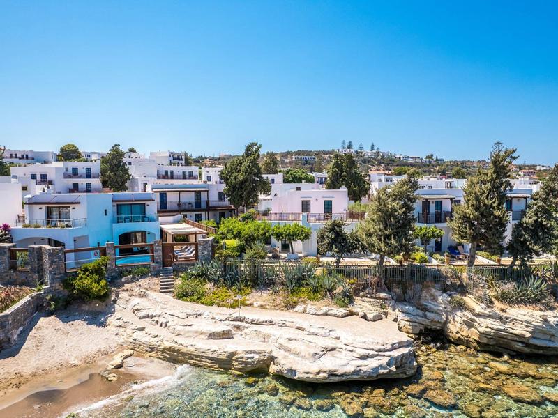 Maisons blanches au bord de la mer avec formations rocheuses et eau claire sous un ciel bleu.