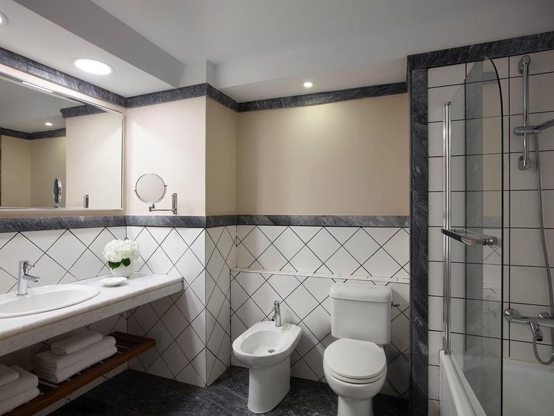 Salle de bain moderne avec toilette, bidet, douche et lavabo sous un miroir éclairé.