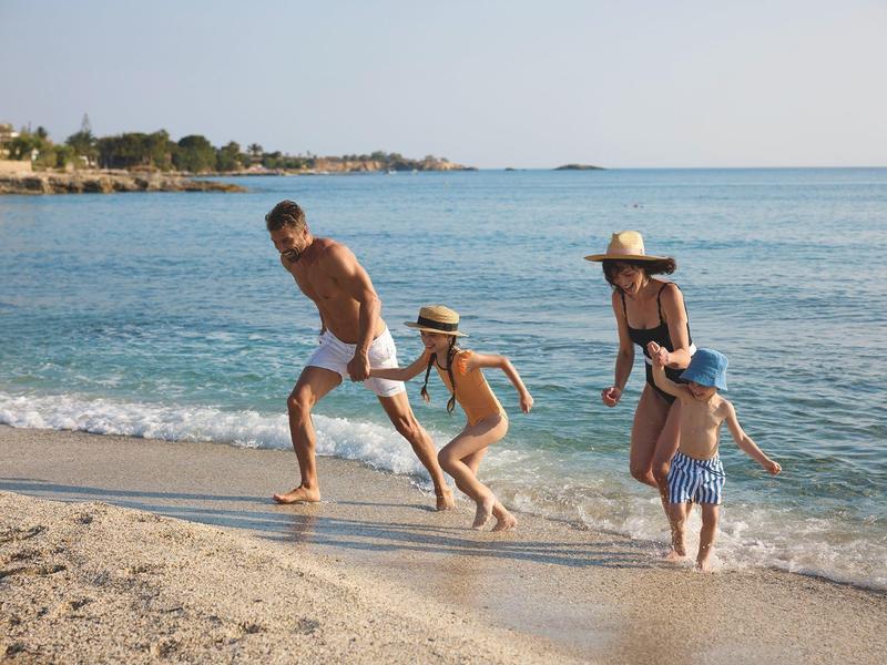 Famille avec deux enfants courant le long de la plage de sable au bord de la mer au soleil.