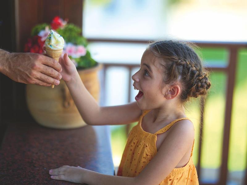 Une fille souriante en robe jaune tenant une glace sur une terrasse.