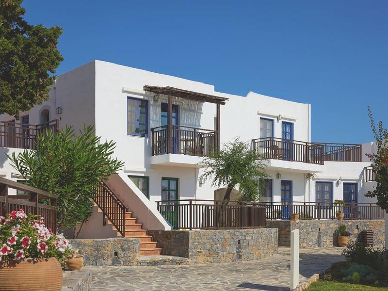 Maison de vacances blanche moderne avec terrasse, jardin et ciel bleu clair.