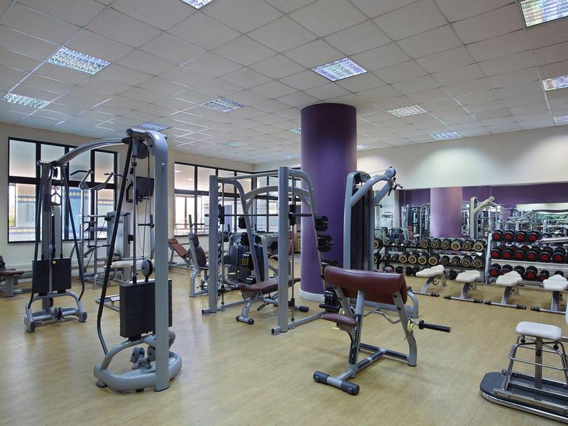 Salle de sport spacieuse avec plusieurs appareils d'entraînement et grands miroirs au mur.
