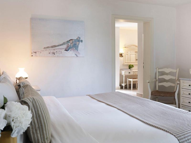 Chambre lumineuse avec grand lit, linge de lit beige et vue sur la pièce adjacente.