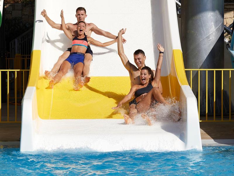 Quatre personnes descendent ensemble un toboggan jaune dans la piscine.