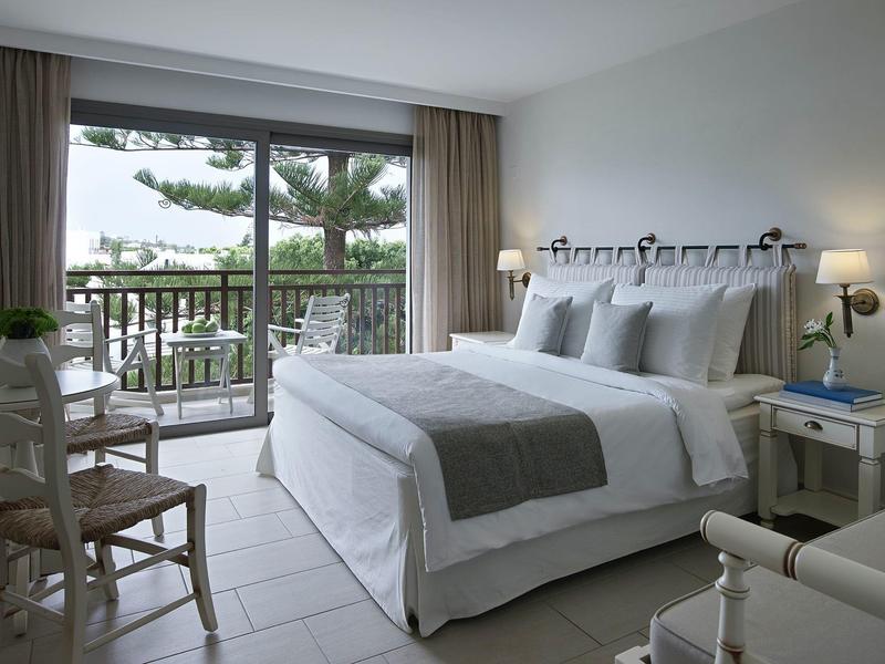 Chambre d'hôtel lumineuse avec grand lit, balcon et vue sur des arbres verts.