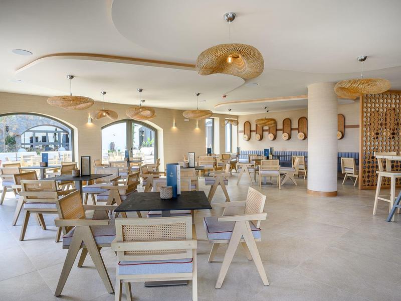 Restaurant d'hôtel lumineux et moderne avec mobilier en bois et grandes fenêtres offrant une vue extérieure.