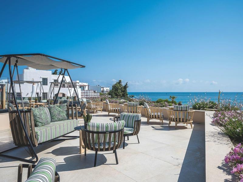 Salon extérieur moderne avec sièges, vue sur la mer et ciel dégagé en arrière-plan.