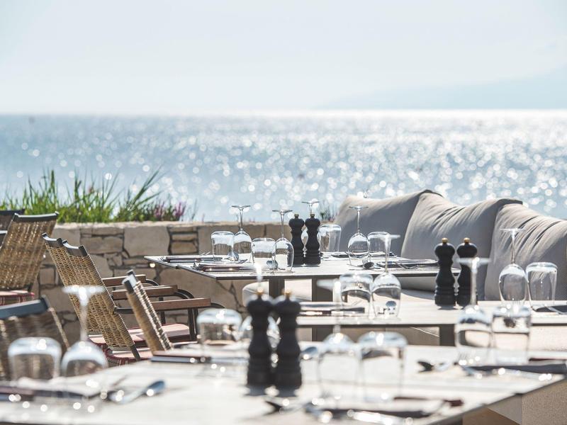 Terrasse extérieure élégante avec tables dressées et vue sur la mer scintillante.