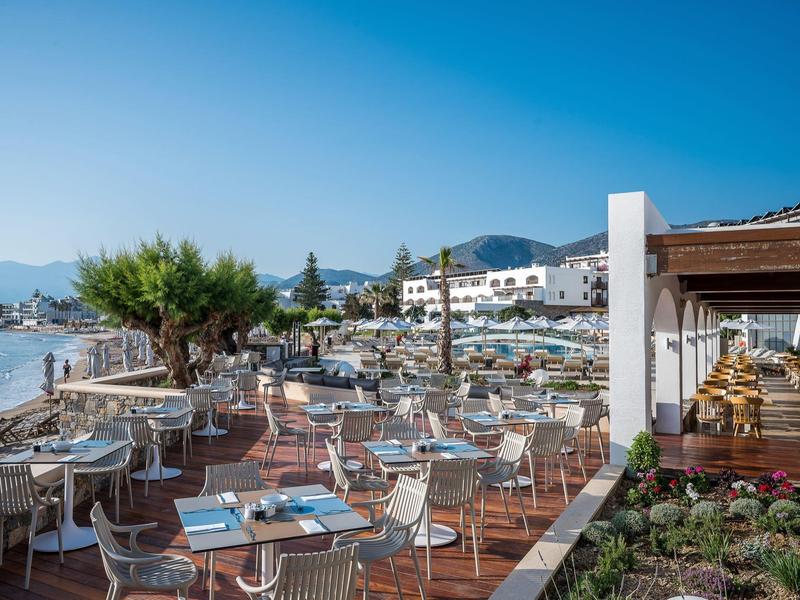 Terrasse ouverte d'un restaurant en bord de mer avec vue sur la mer et le coucher de soleil.