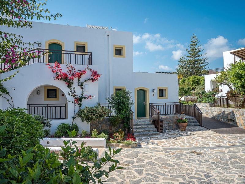 Bâtiment blanc avec des portes vertes et des fleurs sur une surface pavée sous un ciel bleu.