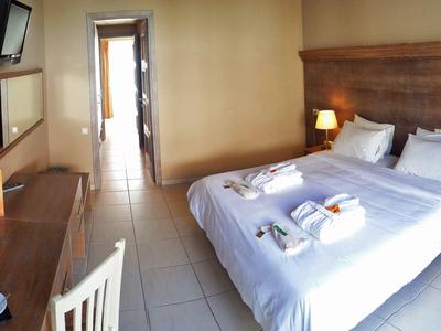 Kleines Hotelzimmer mit Doppelbett, Holzkopfteil, zwei Lampen, Schreibtisch und Spiegel.