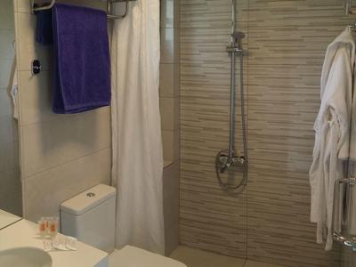 Kleines Badezimmer mit weißen und grauen Fliesen, Toilette, Waschbecken, Duschvorhang und Handtüchern.
