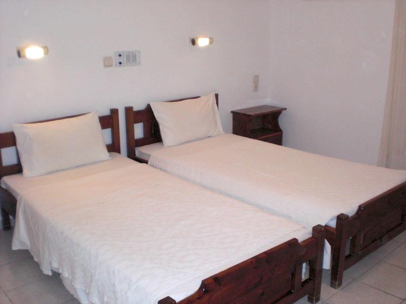 Einfaches Schlafzimmer mit zwei Einzelbetten, weißen Bettdecken und einem kleinen Nachttisch.