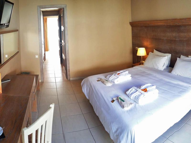 Kleines Hotelzimmer mit Doppelbett, Holzkopfteil, zwei Lampen, Schreibtisch und Spiegel.