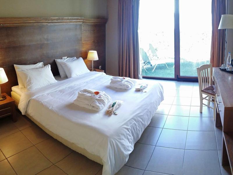 Hell eingerichtetes Schlafzimmer mit einem großen Bett, Nachttischlampen und Balkon im Hintergrund.