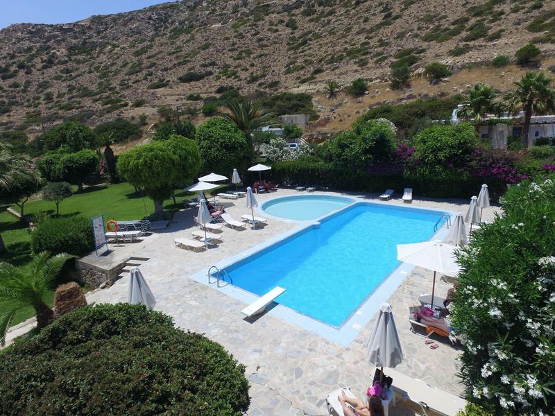 Schwimmbad mit Liegestühlen und Sonnenschirmen, umgeben von grüner Vegetation und Bergen im Hintergrund.