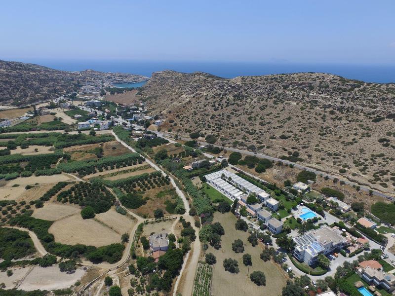 Berglandschaft mit grünen Feldern, Gebäuden und blauem Meer im Hintergrund unter klarem Himmel.
