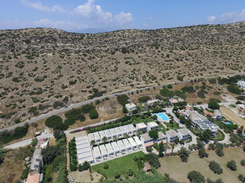 Landschaft mit trockenem hügeligem Terrain, Wohnanlage mit weißen Gebäuden und blauem Pool.