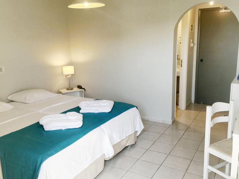 Helles Zimmer mit Doppelbett, grünem Bettläufer, weißen Handtüchern und Zugang zu Bad mit Bogen.