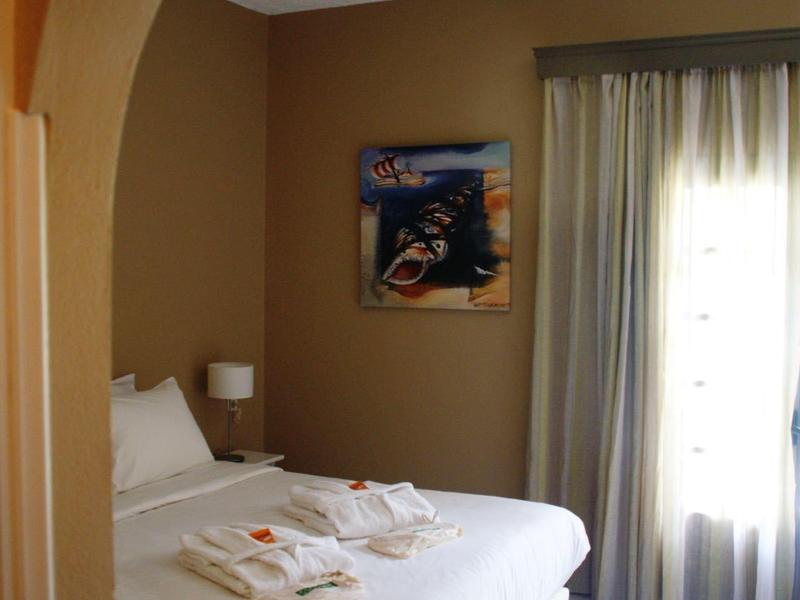 Helles Schlafzimmer mit weißem Bett, Deckenventilator, Vorhängen und Wandbild unter einem Bogen.