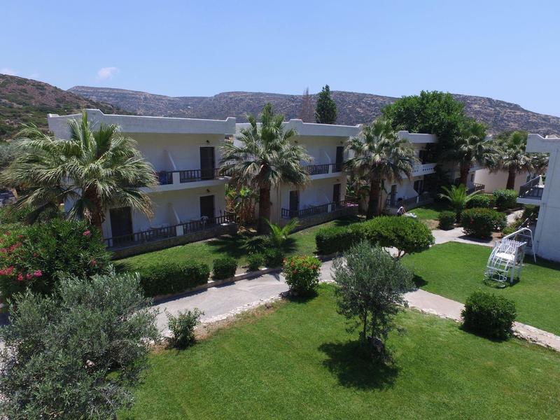 Zweistöckiges Gebäude mit Balkonen, Palmen und gepflegtem Rasen in sonniger Landschaft.