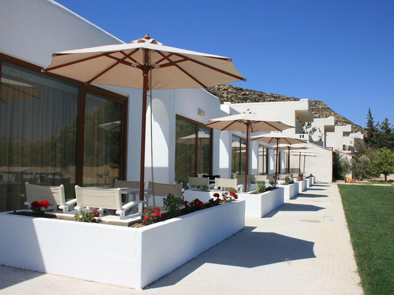 Moderne Terrasse mit weißen Wänden, Sonnenschirmen und grüner Rasenfläche bei klarem Himmel.