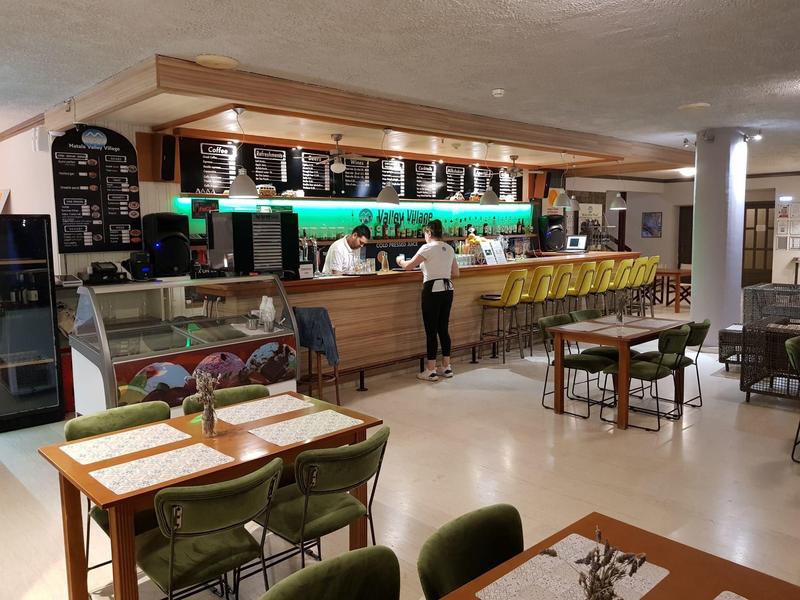 Moderner Caféinnenraum mit Holzbar, grünen Stühlen und gedeckten Tischen, helle Beleuchtung.