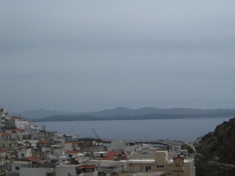 View of a coastal town with sea and mountains in the background under cloudy sky.
