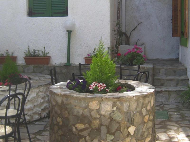 A stone fountain with plants and flowers in a paved courtyard with chairs.