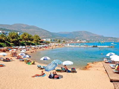 Písčitá pláž s deštníky a lidmi, výhled na moře a hory v pozadí