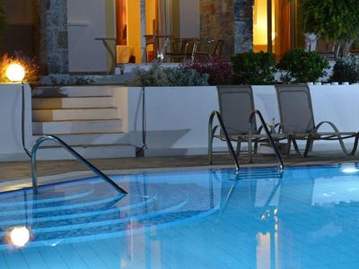 Podświetlany basen przed tarasem z krzesłami w nocy.