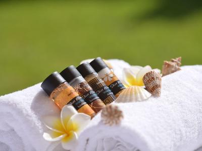 Cztery małe kosmetyki hotelowe na białych ręcznikach ozdobionych muszlami i kwiatami.