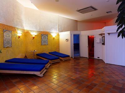 Pokój relaksacyjny z niebieskimi leżakami, żółtymi ścianami i kafelkową podłogą w strefie wellness.