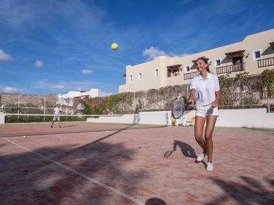 Zwei Frauen spielen Tennis auf einem sonnigen Tennisplatz neben einem Hotel.