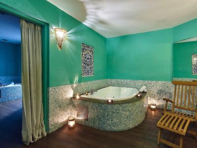 Luksusowa łazienka z zielonymi ścianami, jacuzzi i drewnianym krzesłem w relaksującej atmosferze.