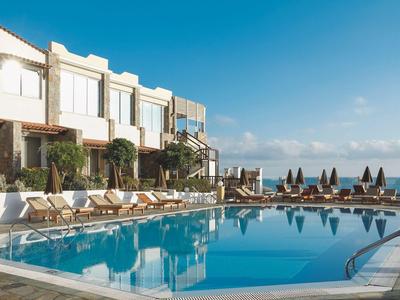 Runder Außenpool mit Liegestühlen vor weißem Hotelgebäude unter klarem Himmel.