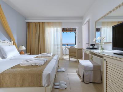 Jasny pokój hotelowy z podwójnym łóżkiem, biurkiem, telewizorem i widokiem na morze przez okno.