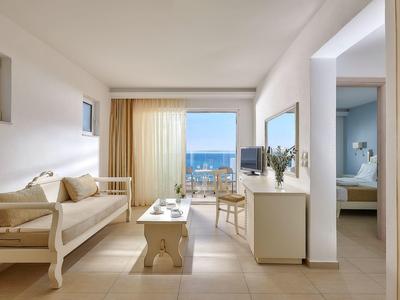 Nowoczesny pokój hotelowy z widokiem na morze, sofą, biurkiem i przyległą sypialnią.