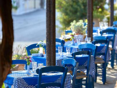 Straßencafé mit blau lackierten Stühlen und karierten Tischdecken neben einer sonnigen Allee.