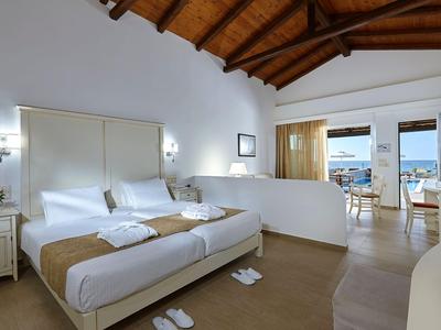 Světý hotelový pokoj se dvojlůžkem, dřevěným stropem a balkonem s výhledem na moře.